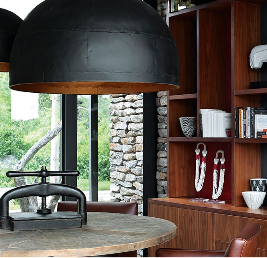 A table with hanging lighting and a bookshelf, surrounded by a glass exterior